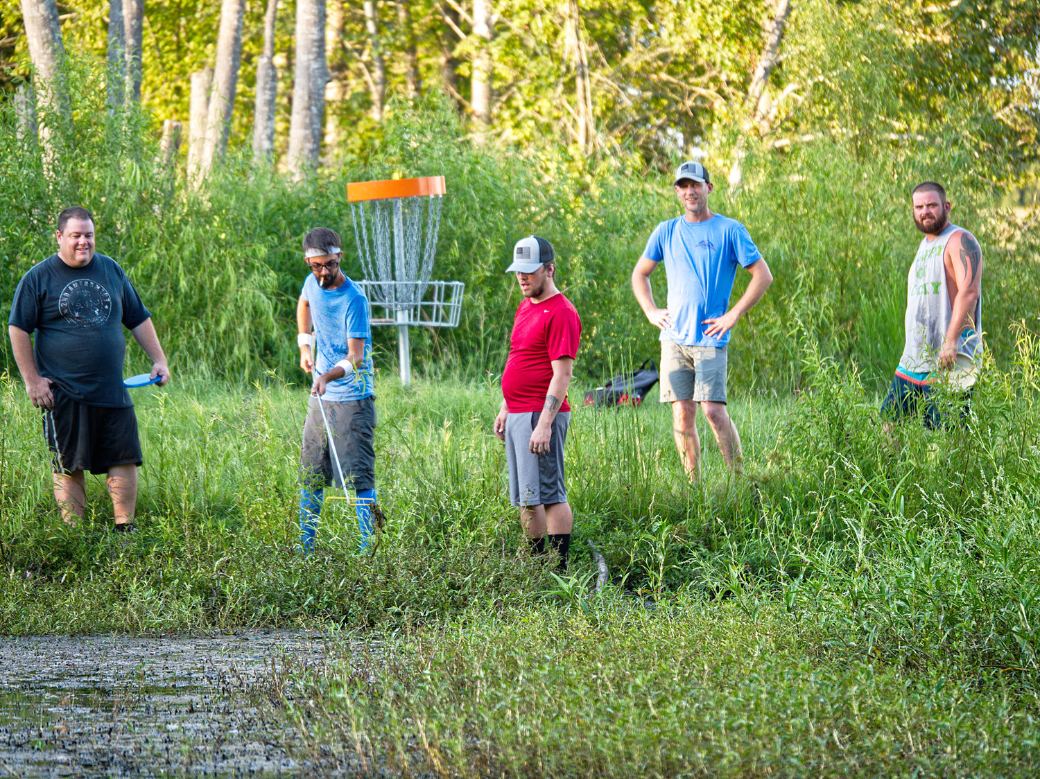 Hooked, Offline, SinkerDisc golfers try to rescue a putter from Grandpa’s Pond next to a hole on The Preserve disc golf course Monday evening at the Mineola Nature Preserve.